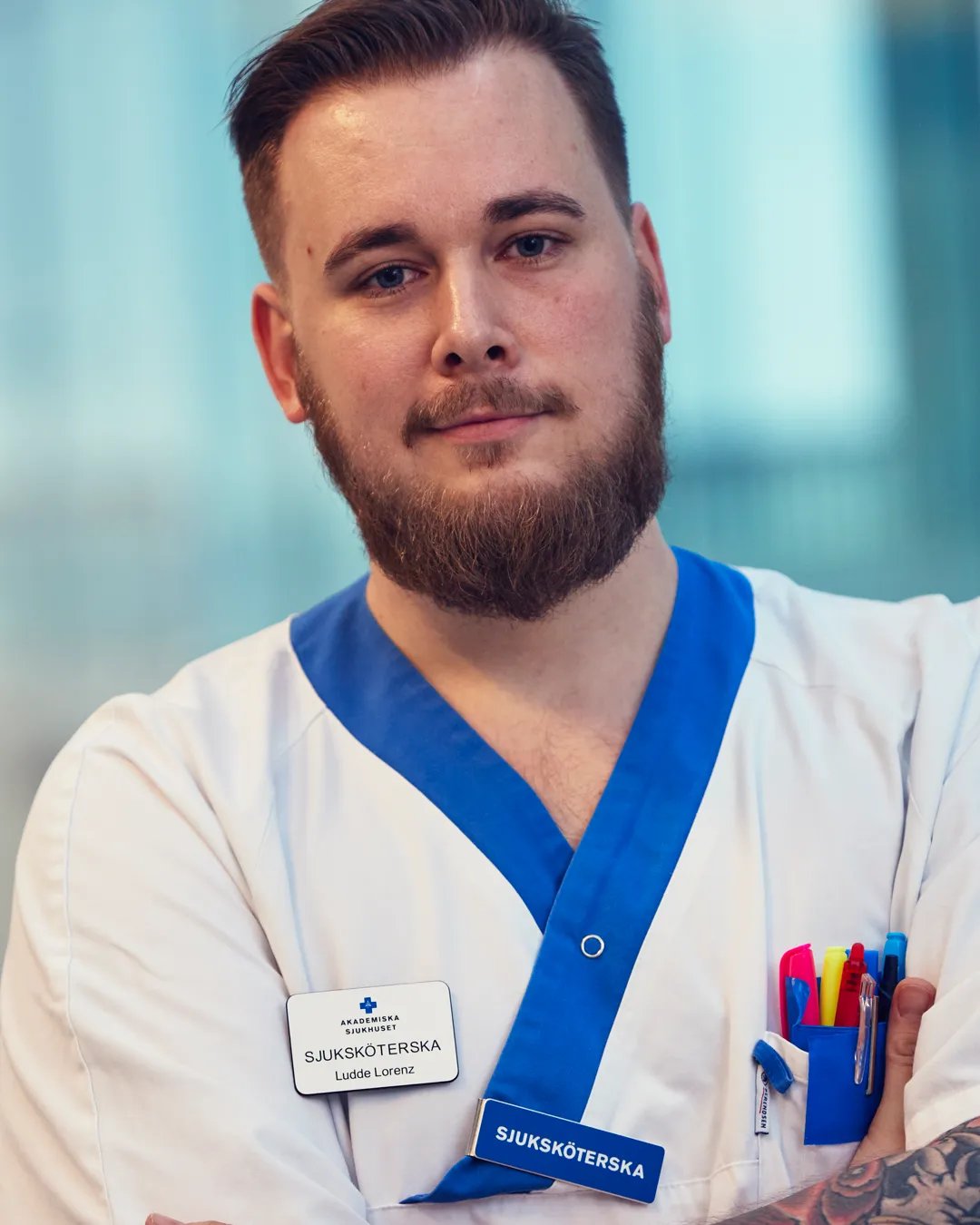 En man med skägg och tatueringar som bär sjukhusuniform.