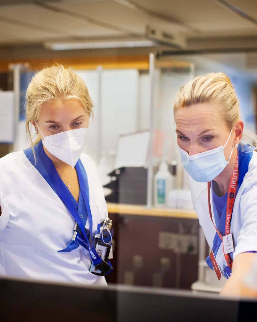 A couple of women wearing face masks working on a computer.