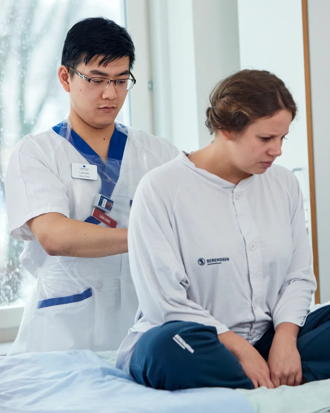 En läkare undersöker en patient som sitter på en sjukhussäng.