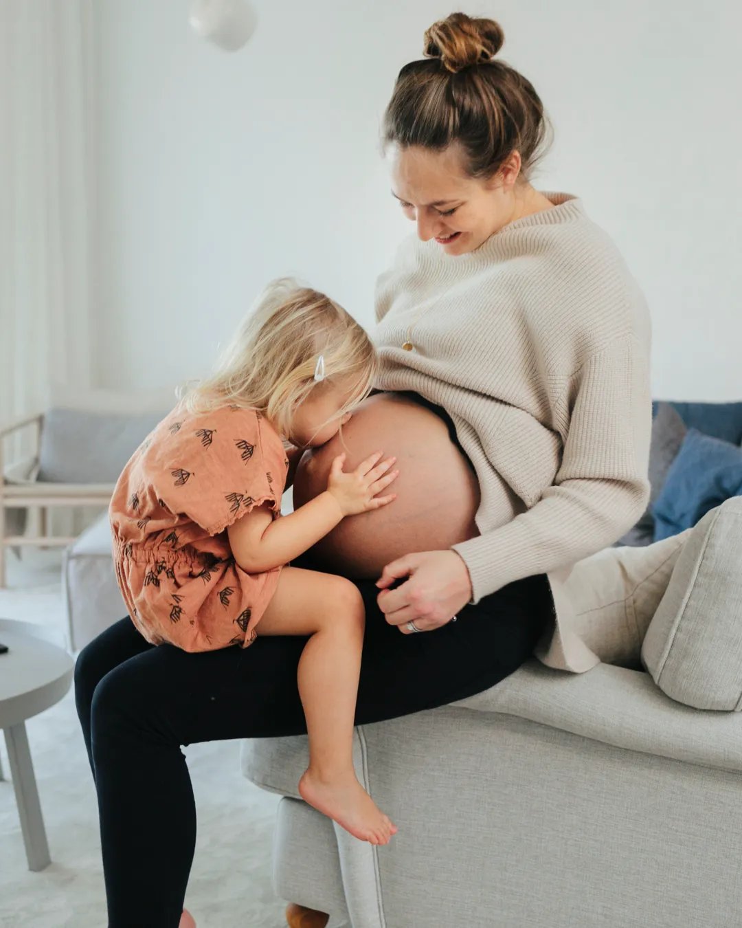 En liten flicka sitter i en gravid kvinnas knä.