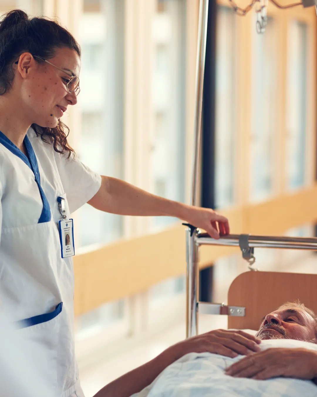 En sjuksköterska skjutsar en patient i en sjukhussäng i en sjukhuskorridor.
