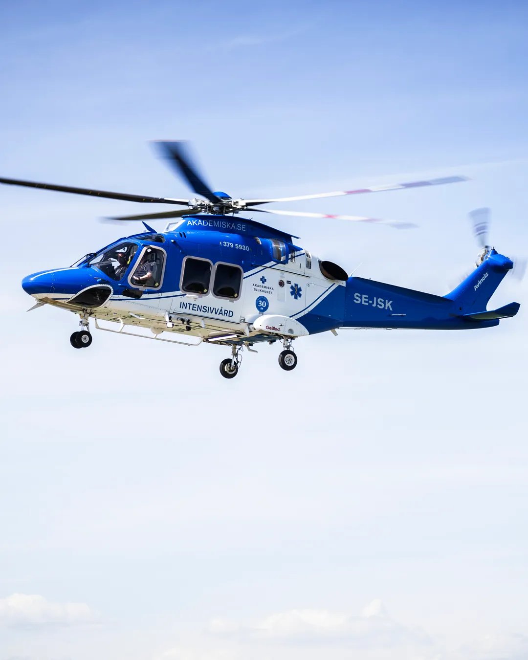 En blå och vit helikopter som flyger på himlen.