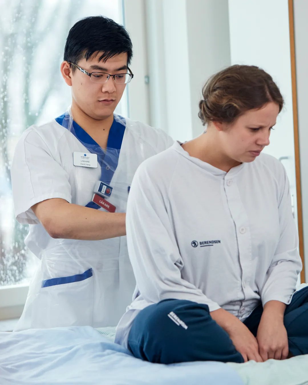 En man i vårdkläder undersöker en patient som sitter på en sjukhussäng.