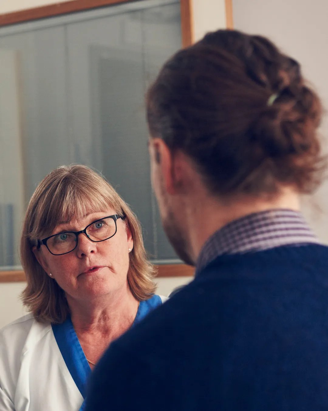 En kvinna i vårdkläder pratar med en patient.