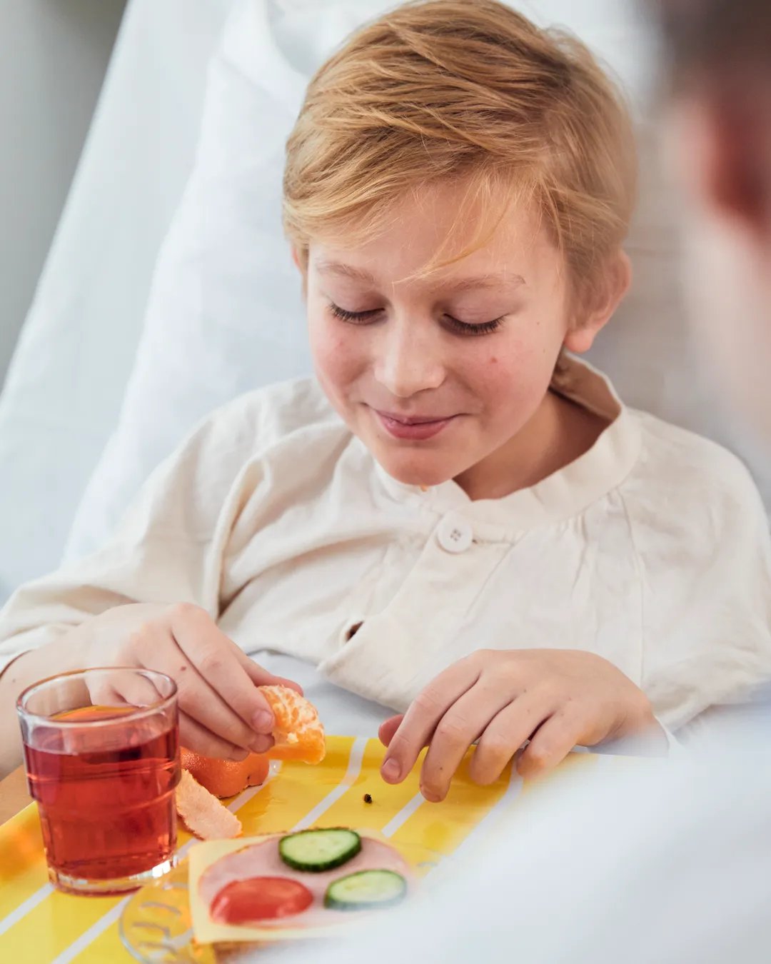 A boy is sitting in a hospital bed with a tray of food.