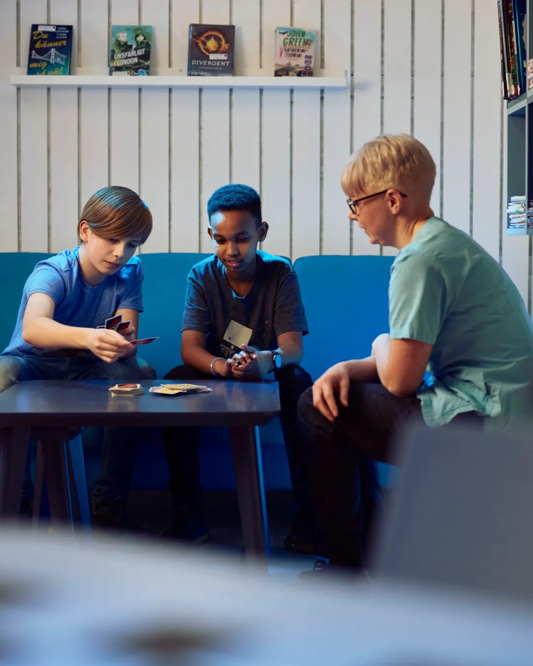 Två pojkar spelar kort med en vuxen i ett tonårsrum.