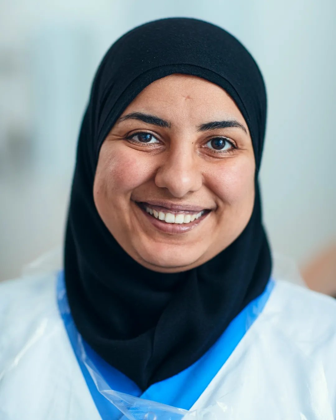 En kvinna i hijab som jobbar inom vården ler mot kameran.
