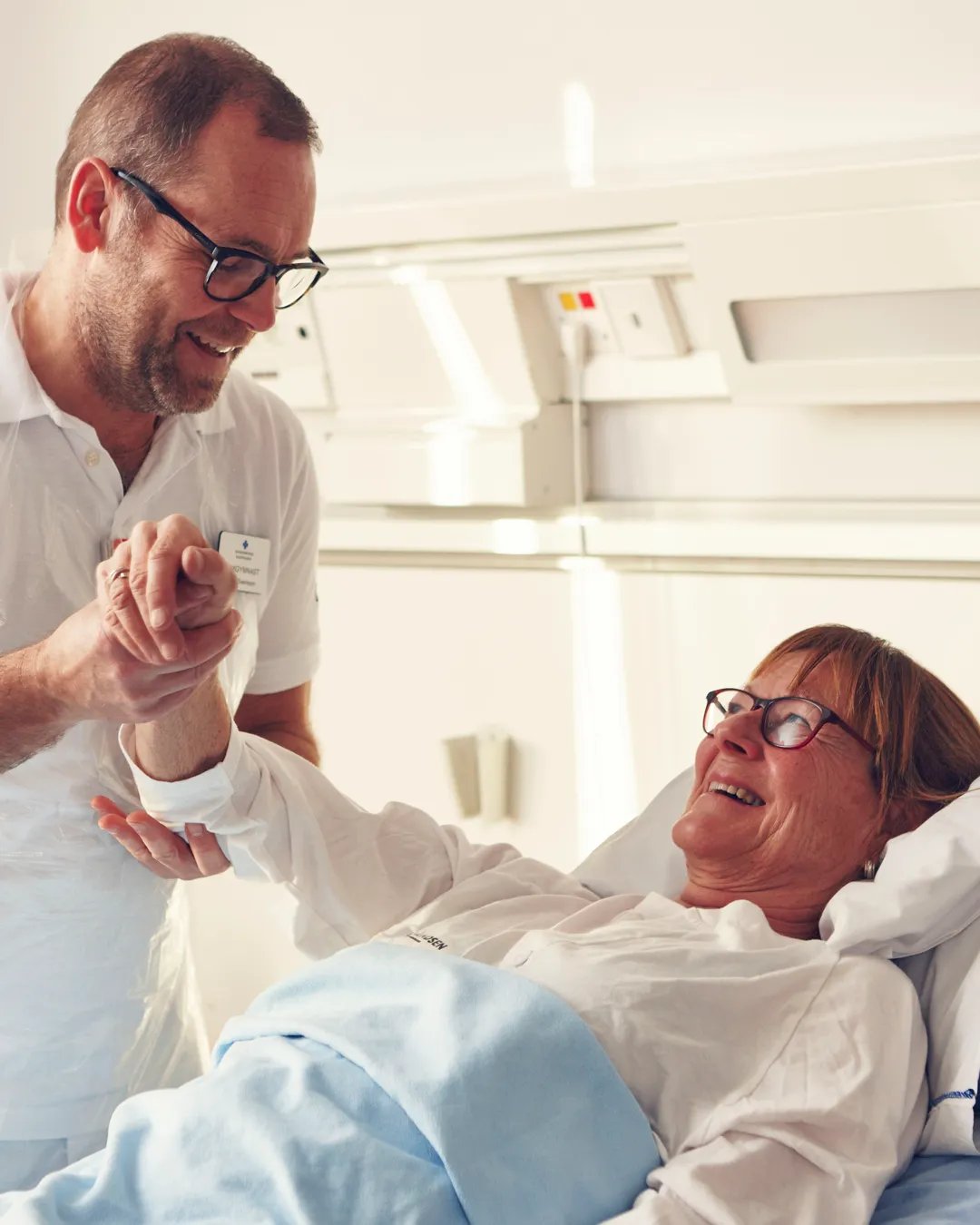 En patient i en sjukhussäng ler mot en läkare.