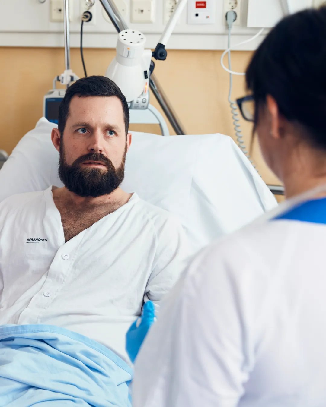 En patient som sitter i en sjukhussäng pratar med en läkare.