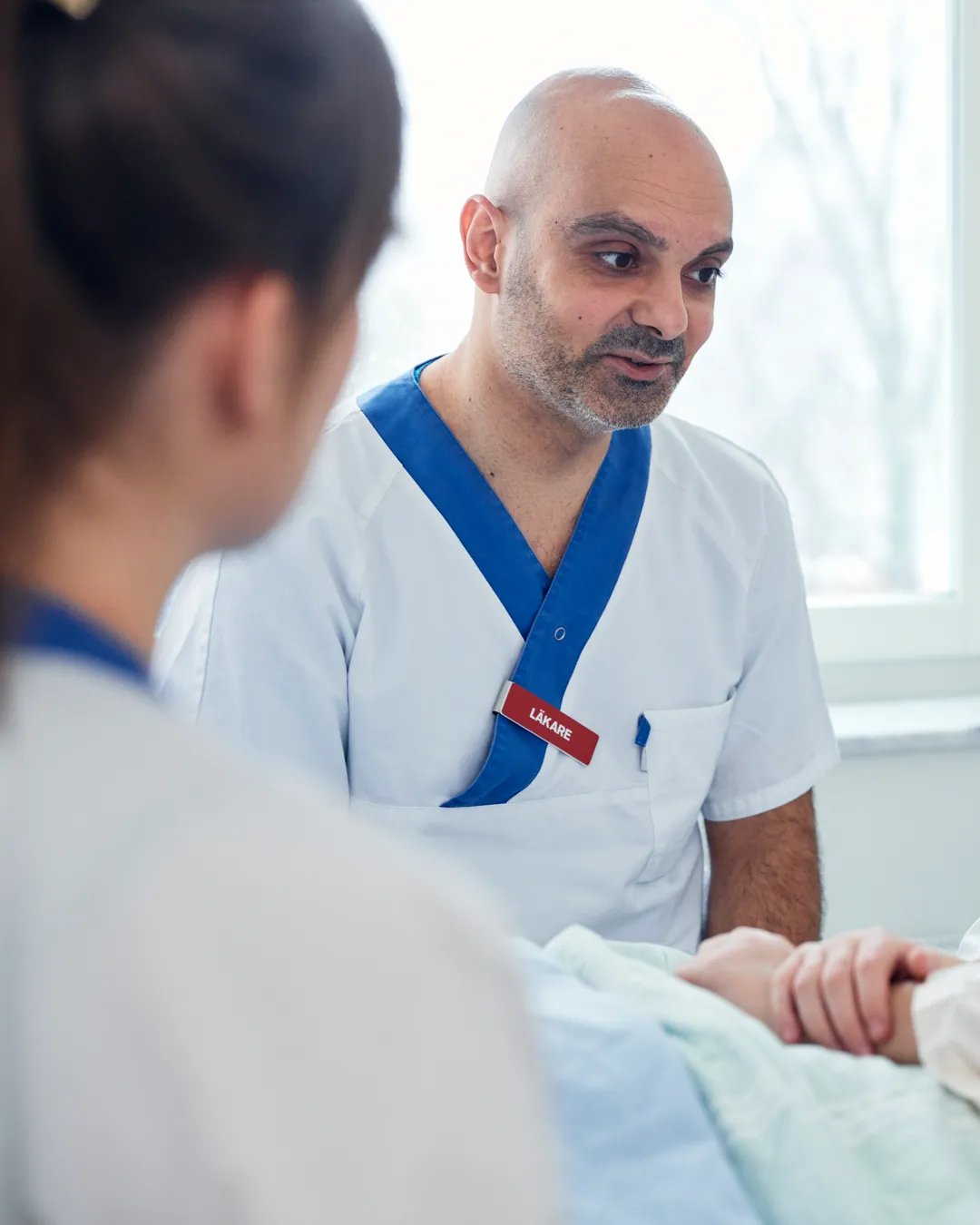 En sjuksköterska pratar med en patient i en sjukhussäng.