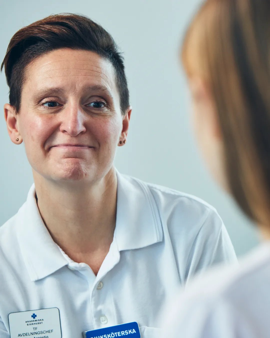 En sjuksköterska pratar med en patient i vit tröja.