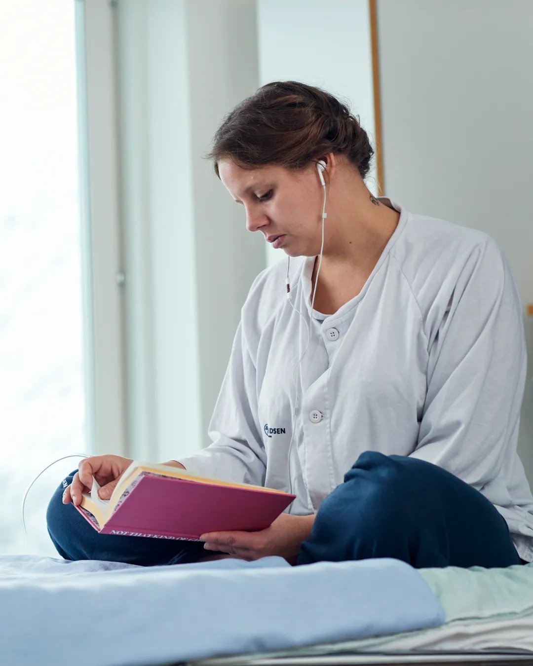 En patient sitter på en sjukhussäng och läser en bok.