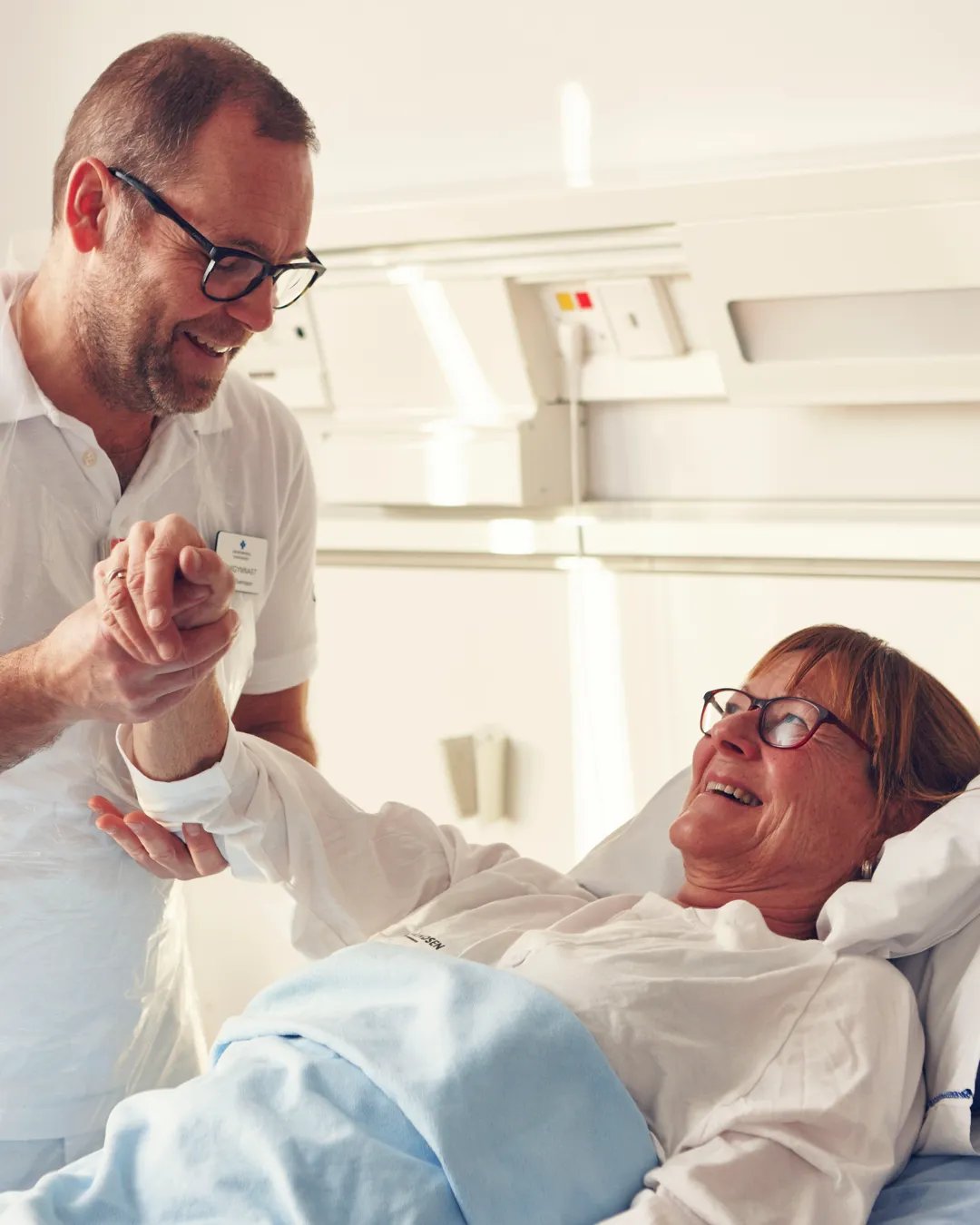En patient i en sjukhussäng får hjälp av en sjuksköterska.