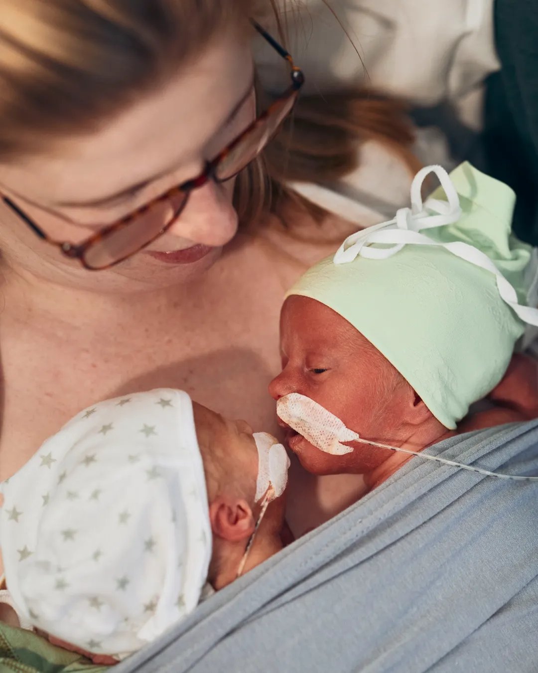 En nybliven mamma håller i sina två nyfödda tvillingar.