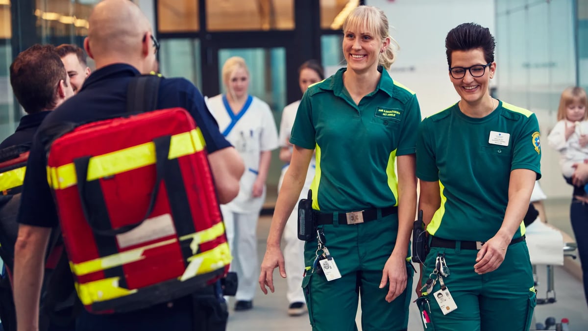Två kvinnliga ambulanssjukvårdare går bredvid varandra och ser glada ut.
