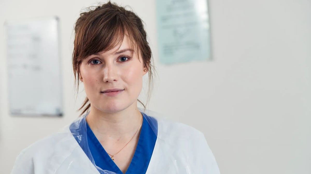 En kvinna i vit labbrock med ett blått band runt halsen.