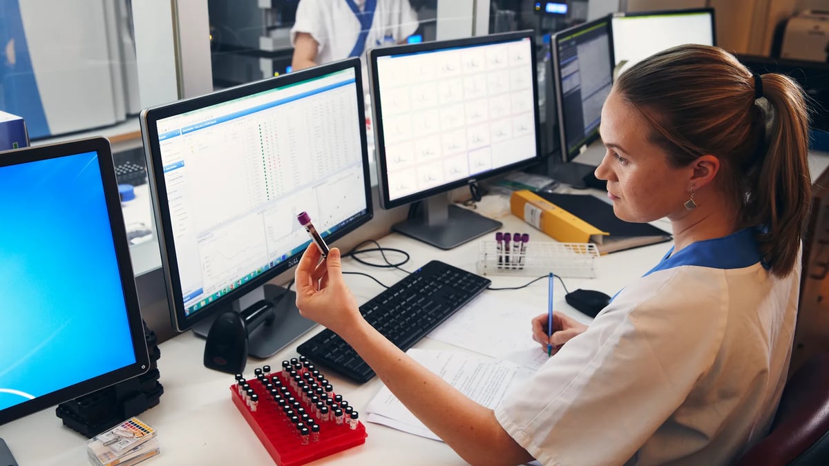 En kvinna sitter vid ett skrivbord framför tre datorskärmar.