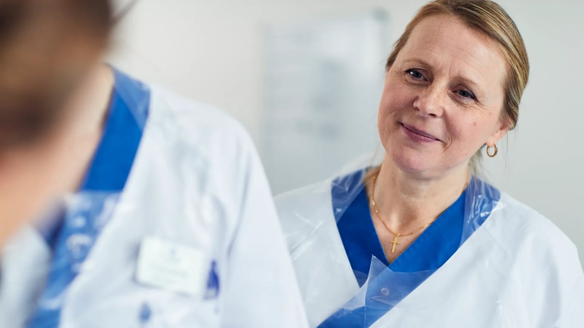 En kvinna i vit labbrock pratar med en annan kvinna.