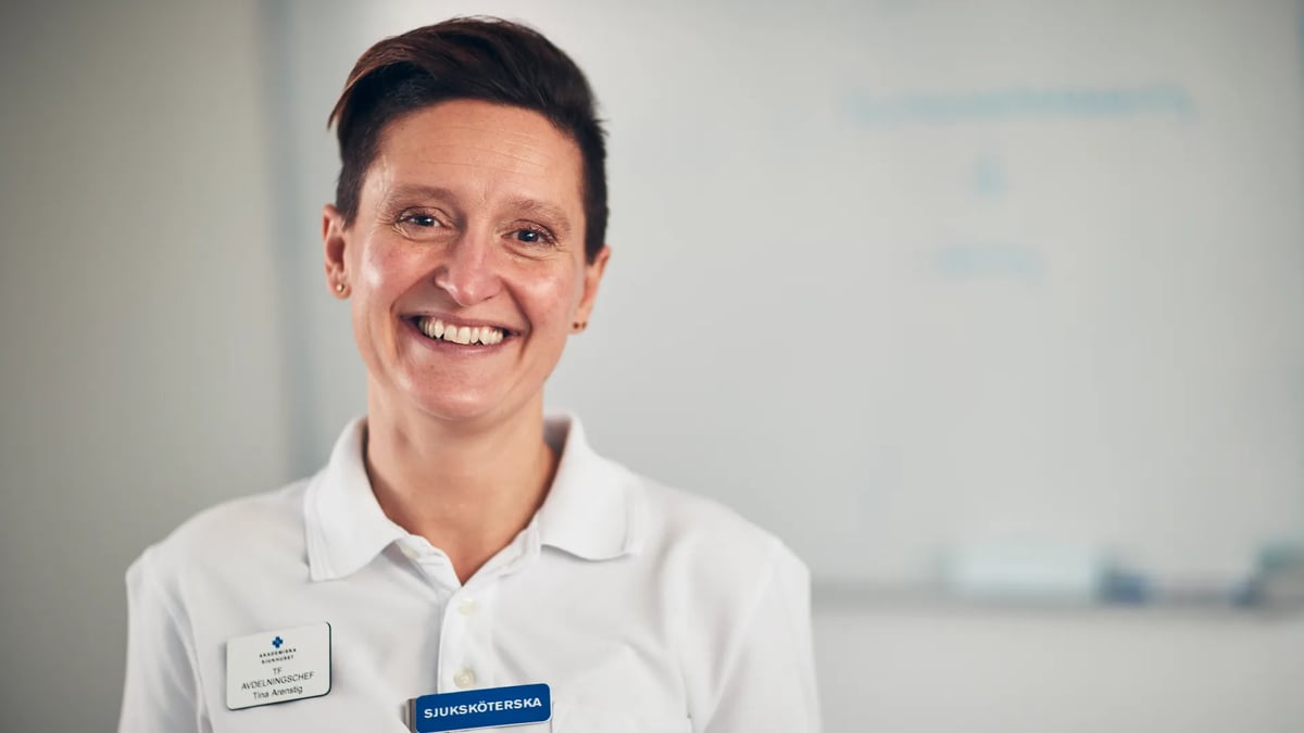 En kvinna i vit skjorta ler mot kameran.