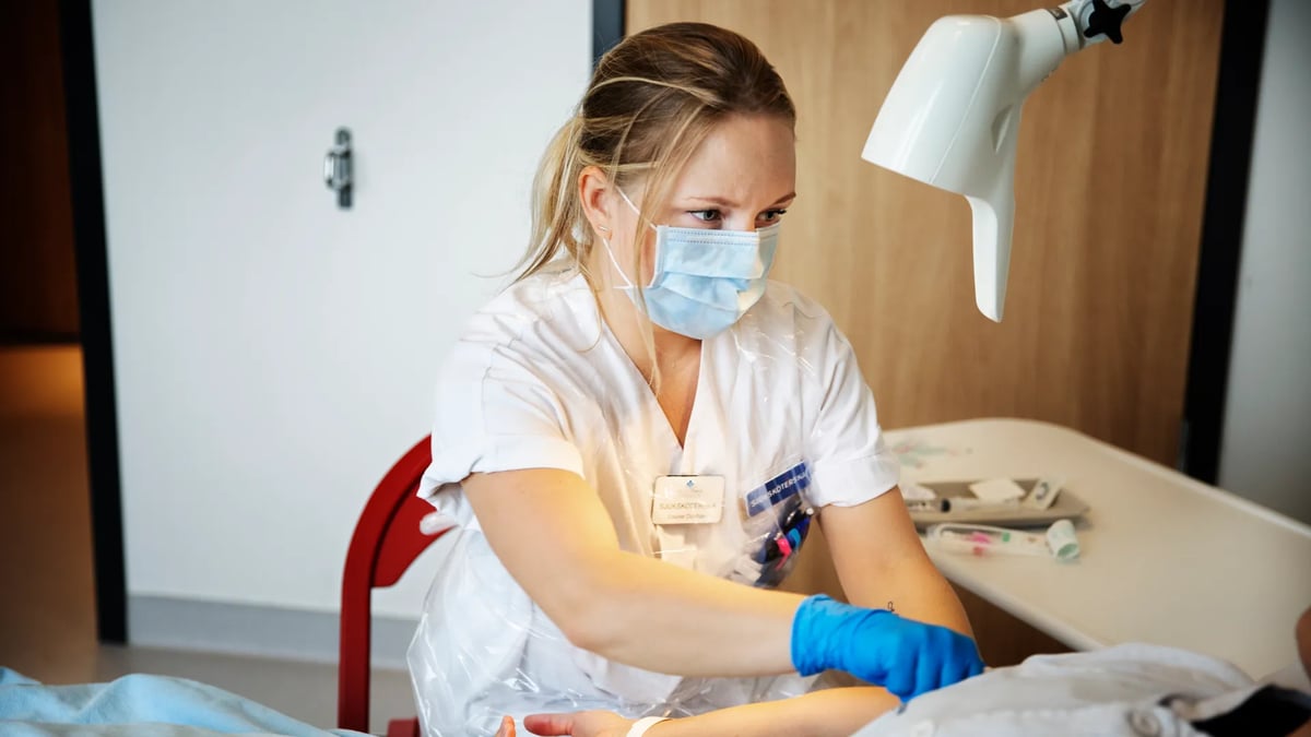 En kvinnlig sjuksköterska i vita arbetskläder behandlar patient.