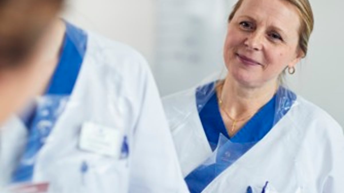 En kvinna i vit labbrock pratar med en annan kvinna.