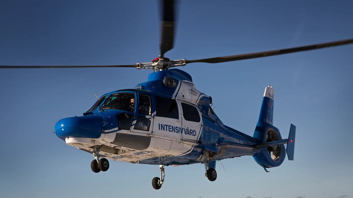 En blå och vit helikopter som flyger över en landningsbana.