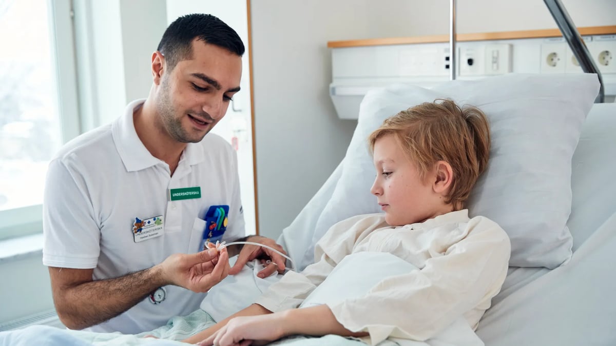 En liten pojke i en sjukhussäng undersöks av en manlig läkare.
