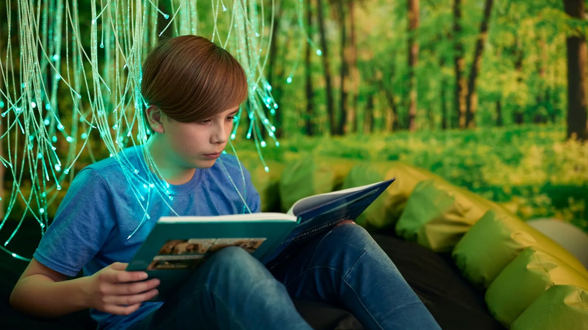 En ung pojke sitter på en soffa och läser en bok.