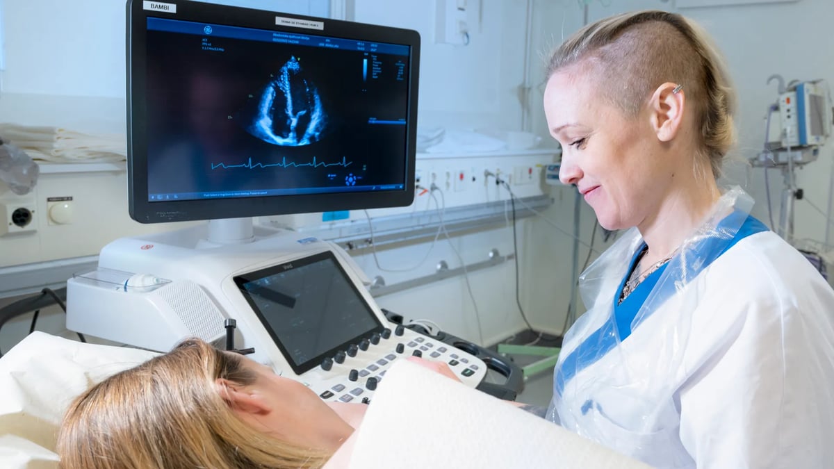 En kvinna ligger i en sjukhussäng bredvid en monitor.