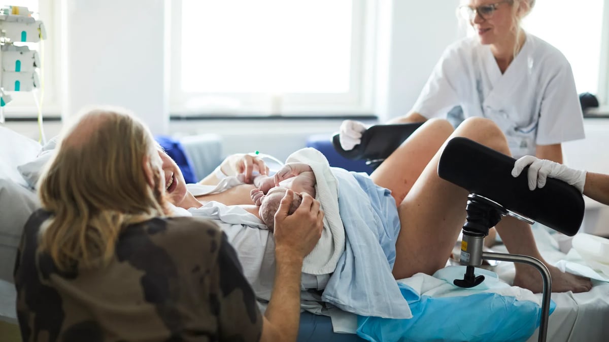 En kvinna som ligger i en sjukhussäng bredvid en sjuksköterska.