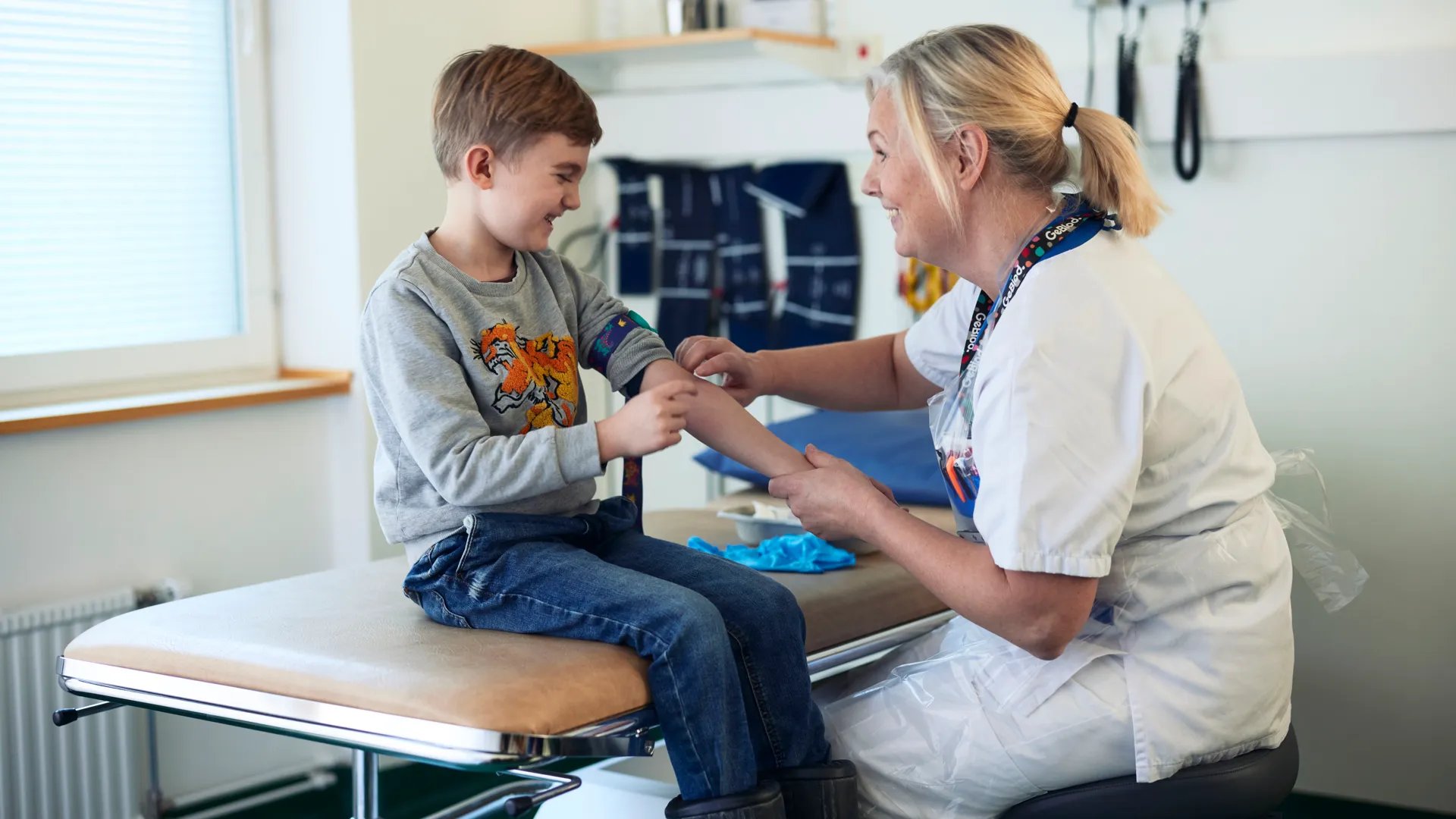Kvinnlig vårdpersonal sitter på en stol bredvid en liten pojke.