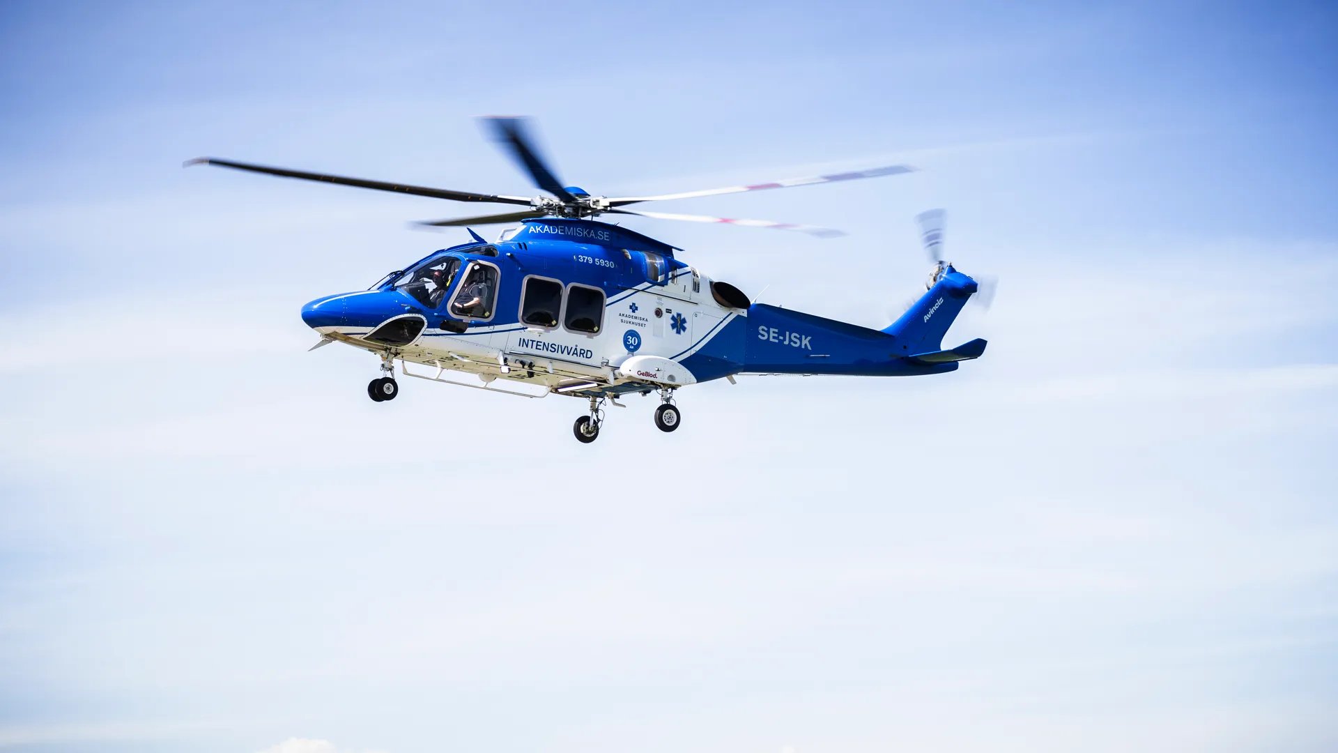 En blå och vit helikopter som flyger på himlen.
