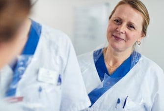 En kvinna i vit labbrock pratar med en annan kvinna.