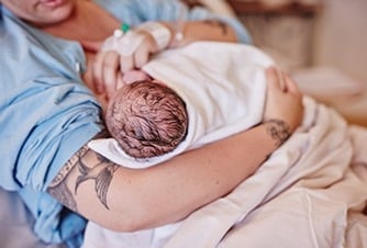En kvinna håller en baby insvept i en filt.