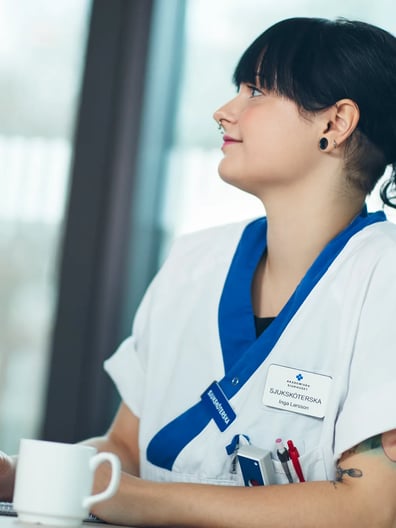 En kvinna i vårdkläder lyssnar och antecknar vid ett bord.