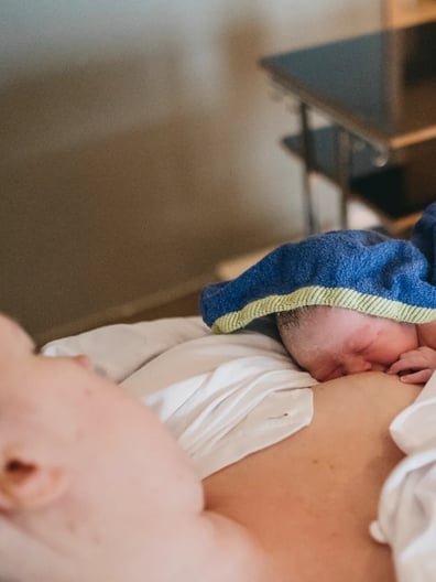 En kvinna som ligger i sängen med en bebis insvept i en filt.