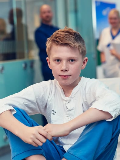 En pojke sitter på en sjukhussäng.