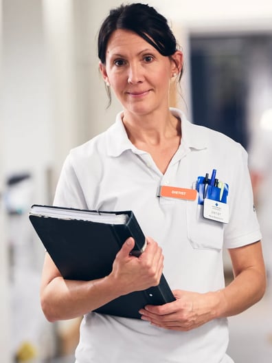 En sjuksköterska håller i en pärm i en sjukhuskorridor.