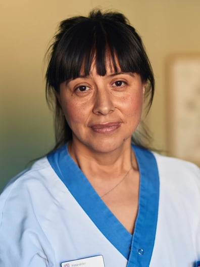 En kvinna i vårdkläder ler mot kameran.