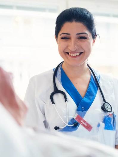 En läkare ler mot en patient som ligger i en sjukhussäng.