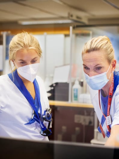 A couple of women wearing face masks working on a computer.