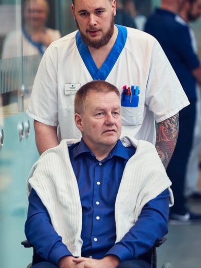 En man blir skjutsad i en rullstol av en sjuksköterska.