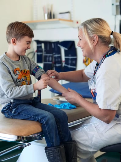 Kvinnlig vårdpersonal sitter på en stol bredvid en liten pojke.