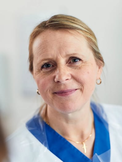 A woman in a white coat smiles at the camera.