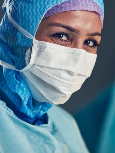 En kvinna har kirurgmask och operationskläder på sig.