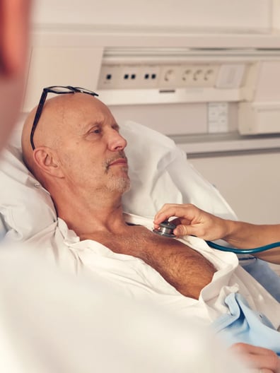 En man i en sjukhussäng undersöks av en sjuksköterska.