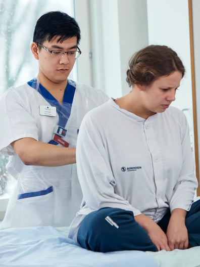 En läkare undersöker en patient som sitter på en sjukhussäng.