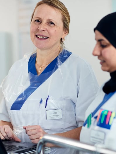 Två kvinnor i operationskläder tittar på en bärbar dator.