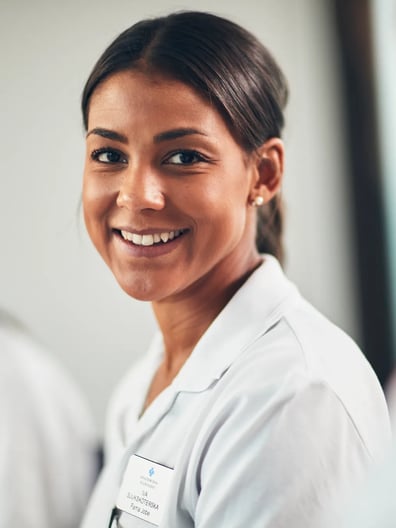 En kvinna i vit labbrock ler mot kameran.