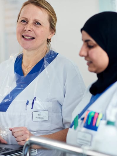 Två kvinnor i operationskläder tittar på en bärbar dator.